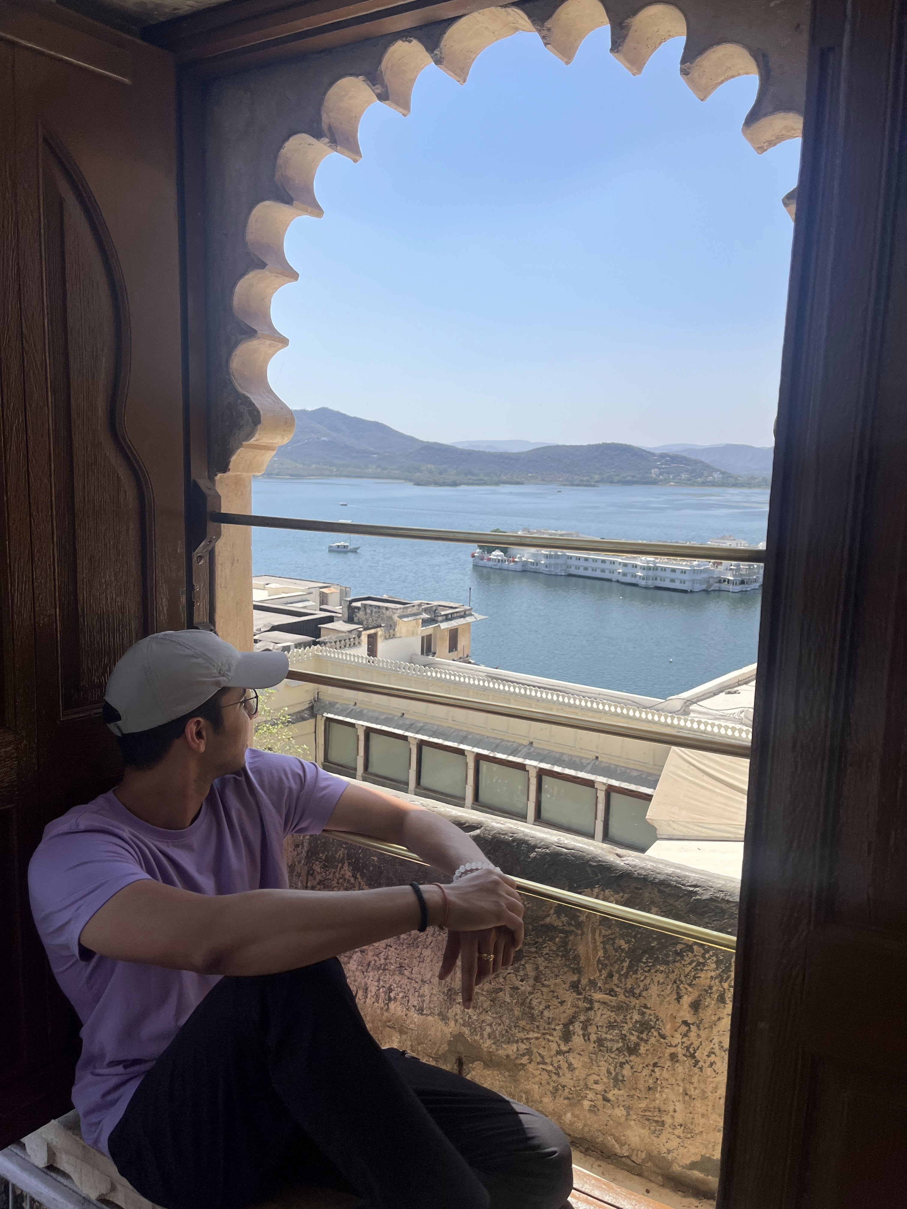 Jai sitting by a window looking out at a lake palace